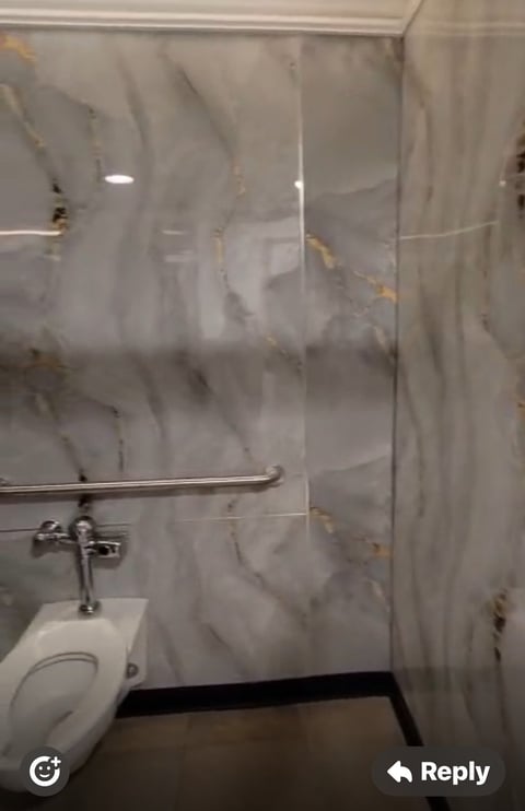 Bathroom shower stall with marble-effect tiled walls, metal showerhead holder, and partial view of white toilet