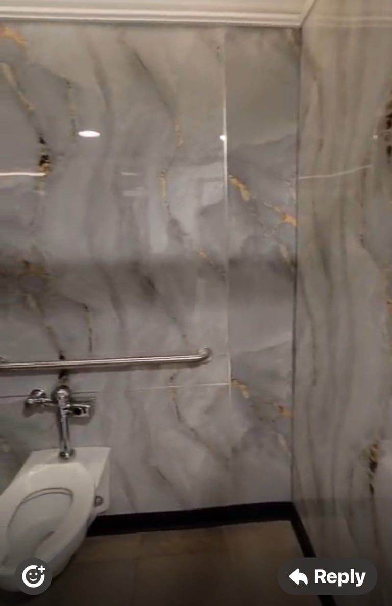Bathroom shower stall with marble-effect tiled walls, metal showerhead holder, and partial view of white toilet