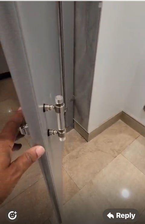 Close-up of a hand holding open a grey door with chrome handle in a tiled bathroom or hallway