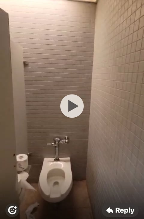 Small bathroom toilet stall with white ceramic toilet, metal flush valve, and tiled walls in neutral tones