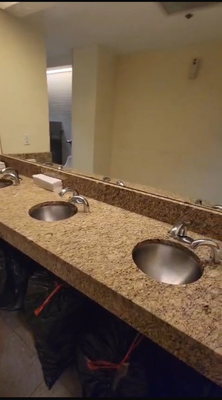 Commercial bathroom vanity with granite countertop, two round stainless steel sinks, chrome faucets, and large mirror with overhead lighting