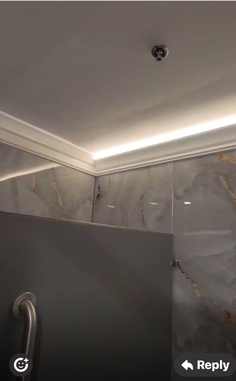 Modern bathroom with glass shower enclosure, recessed ceiling lights, and metallic grab bar on tiled walls