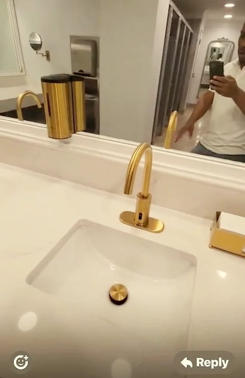 Modern bathroom sink with gold faucet and fixtures, white vanity, and mirror reflecting person taking selfie