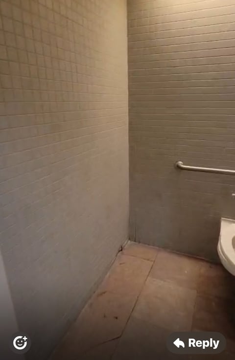Empty bathroom corner with beige subway tile walls, concrete floor, white toilet, and metal grab bar