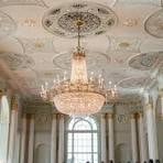 Ornate grand hall with baroque ceiling frescoes, crystal chandelier, and classical columns